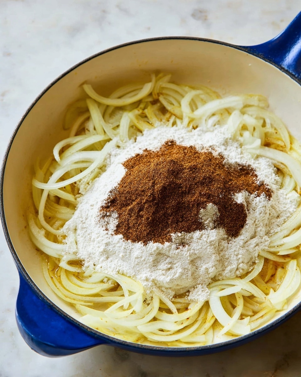 In a white pan with a blue handle, there are thinly sliced yellow onions spread around the edges. In the center, there is a pile of white flour and a heap of dark brown spice powder sitting over the onions. The onions look soft and slightly cooked, with a bit of light yellow from oil. The pan is placed on a white marbled surface. photo taken with an iphone --ar 4:5 --v 7