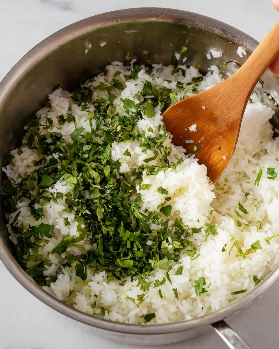 A close-up view of a metal pot filled with white cooked rice as the base layer, topped with fresh light and dark green chopped herbs scattered unevenly across the rice. A woman's wooden spoon is partially inside the pot, resting on the right side, stirring the ingredients. The pot sits on a white marbled surface. Photo taken with an iphone --ar 4:5 --v 7
