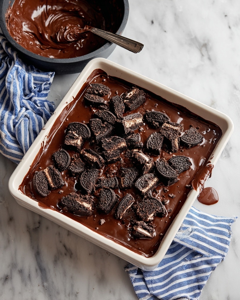 The image shows two square chocolate brownies on a white plate with a white marbled background. Each brownie has three visible layers: the bottom layer is a rich dark chocolate brownie base with a slightly rough texture, the middle layer looks creamy and light beige, likely a cheesecake or cream layer, and the top layer is smooth, glossy dark chocolate ganache with chunky pieces of crushed dark chocolate cookies scattered unevenly on top. The brownies are cut into neat squares with clear edges and crumbs are visible around them. Photo taken with an iphone --ar 4:5 --v 7
