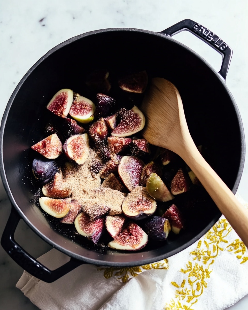 The image shows a close-up of a fresh fig and a jar of fig jam on a soft light pink cloth with some text. The fig is purple with a green stem, sitting near the jar which is filled with thick, shiny, golden-brown fig jam. In front, two halves of a fig reveal their juicy, pinkish-red interior with tiny yellow seeds, and a spoon coated with sticky jam lies nearby with some jam spilled on the cloth. The background is a white marbled texture, softly blurred, giving focus to the fruit and jam in the front, photo taken with an iphone --ar 4:5 --v 7