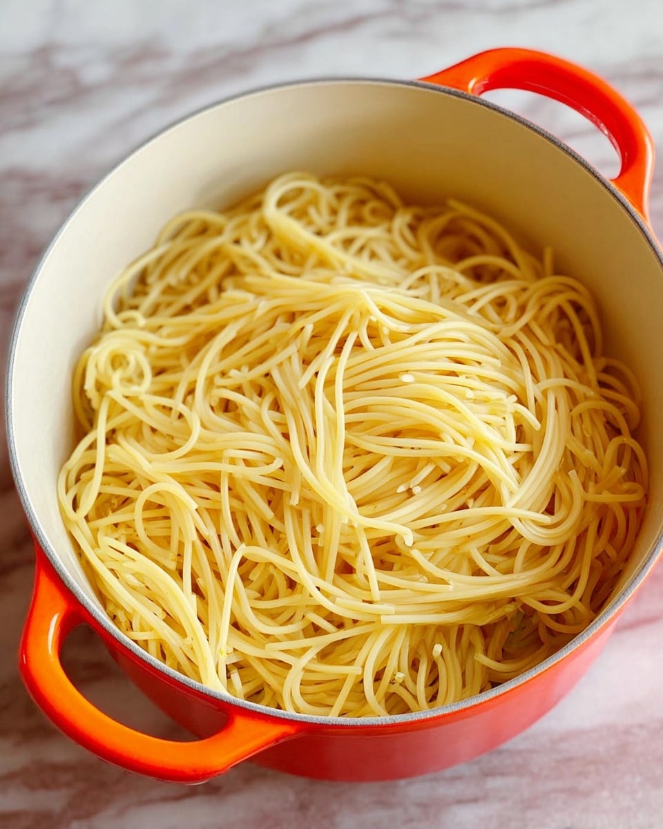 A thick layer of chunky red meat sauce with visible bits of onion and tomato sits on top of a base layer of pale yellow pasta or noodles, all inside a round white pot with orange handles. The meat sauce has a textured, uneven surface and covers the pasta below completely. The pot is placed on a white marbled surface. Photo taken with an iphone --ar 4:5 --v 7