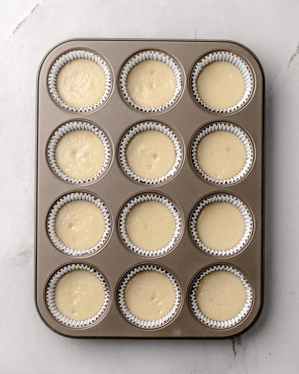 The image shows a group of cupcakes on a white plate, placed on a white marbled surface. Each cupcake has three visible layers: the bottom is a purple paper liner, the middle is a light yellow cake layer, and the top is a swirl of white cream frosting. On top of the frosting, there is a dark purple blueberry sauce drizzle, and the cupcakes are crowned with three fresh blueberries each. Some loose blueberries are scattered around the plate, adding to the visual appeal. Photo taken with an iphone --ar 4:5 --v 7