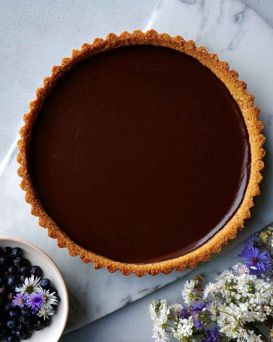 A round tart with a dark, smooth chocolate filling forms the center layer, surrounded by a thick, crumbly dark crust. On the top edge of the chocolate layer, there is a ring of chopped green pistachios mixed with whole red raspberries evenly spaced around the tart. Small flakes of salt are sprinkled lightly over the glossy chocolate surface. The tart is placed on a white plate, resting on a white marbled surface with scattered chopped pistachios nearby. To the side, a white plate holds broken dark chocolate pieces, and in the upper left corner, stacked white plates with two gold spoons are visible. Photo taken with an iphone --ar 4:5 --v 7