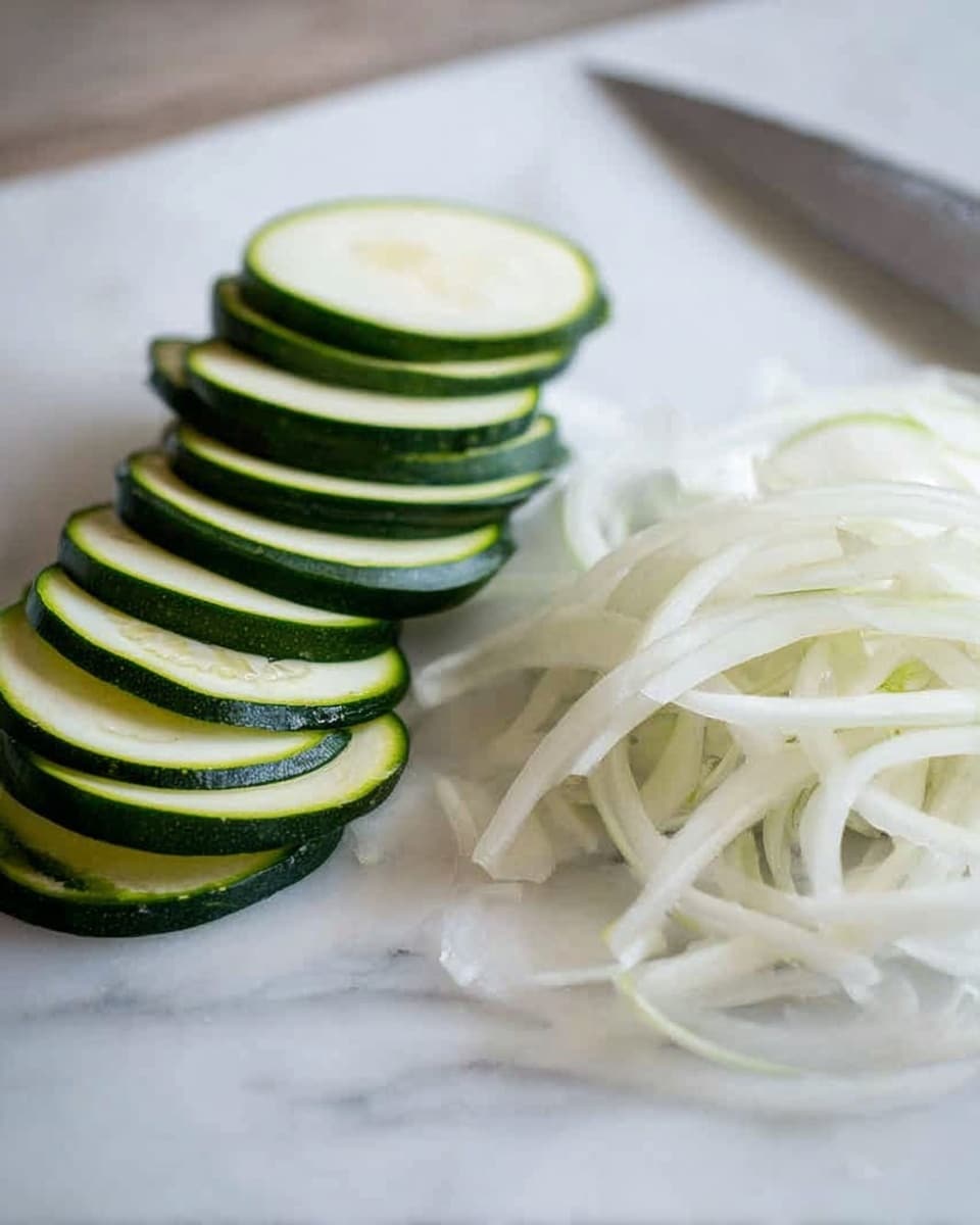 The image shows two piles of sliced vegetables on a white marbled surface. On the left side, there are several thin, round slices of green zucchini arranged in a neat stack, showing the dark green skin and pale green inside. On the right side, there is a small pile of thin, white, long strips of onion, loosely piled and varying in length. In the background, a silver knife is visible on the right side, partly out of focus. Photo taken with an iphone --ar 4:5 --v 7
