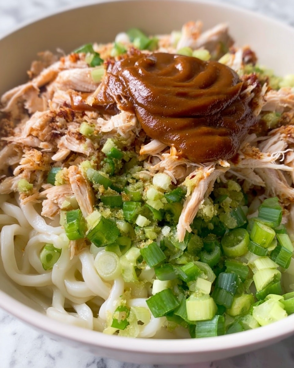 A close-up view of a white bowl filled with thick, creamy noodles mixed with small pieces of browned meat and green vegetables, likely scallions or herbs, spread evenly throughout. The noodles are coated in a light sauce, giving them a slightly shiny texture. The dish is topped with a generous sprinkle of toasted sesame seeds, adding a textured, golden-brown layer on top. A gold fork is stuck into the noodles, lifting some strands, with the tines partially visible. The bowl sits on a white marbled surface. photo taken with an iphone --ar 4:5 --v 7