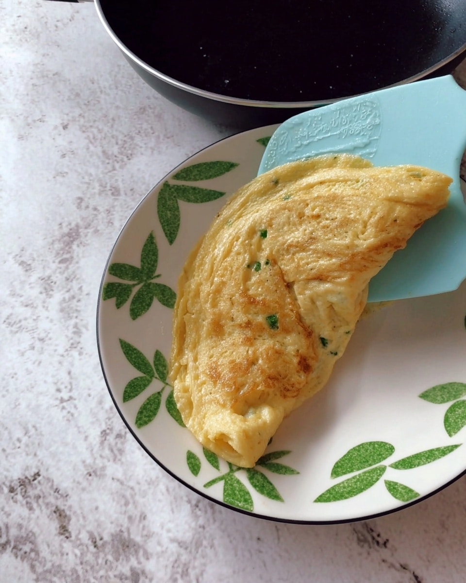 The dish is shown on a white plate with a green leaf pattern around the edge, placed on a white marbled surface. It has three main layers: at the bottom, there is a folded, light yellow omelet with a soft and slightly bumpy texture; on top of that are thin slices of pink-orange smoked salmon arranged loosely; over the salmon, there is a dollop of white creamy cottage cheese that looks smooth and thick. The whole dish is sprinkled with small green chopped chives and small black pepper spots. A lemon wedge with bright yellow flesh and a sprig of fresh green parsley rest at the top side of the plate. A silver fork lies diagonally on the left bottom edge of the plate with its tip touching the omelet. photo taken with an iphone --ar 4:5 --v 7