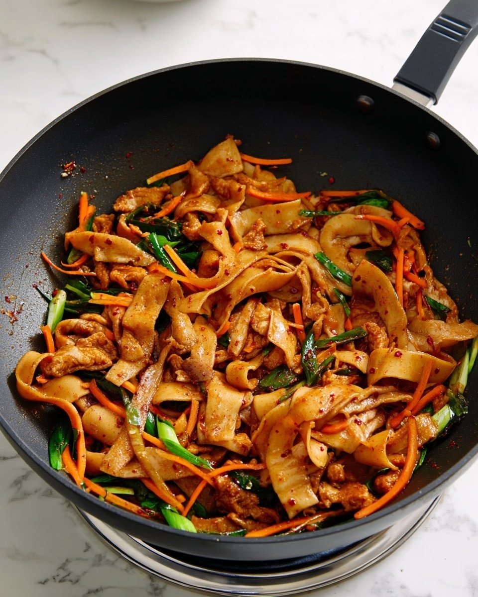 A black pan holds a stir-fry with three main layers: wide, flat light brown strips with a slightly curled shape, thin orange carrot sticks creating a textured middle layer, and dark green onion pieces scattered throughout. The stir-fry has a glossy appearance with some red seasoning showing on the ingredients. The pan is placed on a metallic burner set on a white marbled surface. photo taken with an iphone --ar 4:5 --v 7