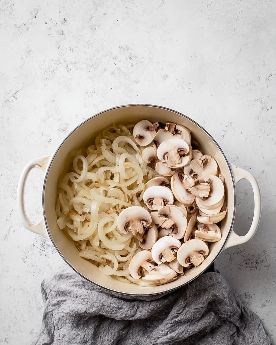 A white pot with two handles sits on a white marbled surface, half filled with soft, translucent, cooked onion slices on the left side and fresh, pale beige and white sliced mushrooms on the right side, showing a contrast between the light brown edges of onions and the smooth mushroom caps; a gray cloth is partially visible below the pot. Photo taken with an iphone --ar 4:5 --v 7
