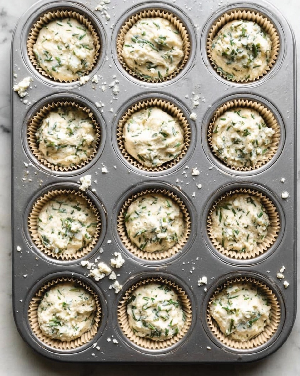 Savory Olive Oil Muffins with Feta, Dill, and Lemon Recipe 5 The image shows a wooden board on a white marbled surface with cooking ingredients neatly arranged. On the board, there is a white bowl filled with white flour mixed with black pepper at the bottom right, and above it is a gray bowl with crumbly white cheese. Two pale blue eggs sit between these bowls, and to the left is a small bunch of fresh green dill. To the far left on the white marbled surface is a dark green bottle labeled extra virgin olive oil, and above it, a white bowl holds four yellow lemons. Another large white bowl filled with a creamy white liquid is placed at the top right corner of the wooden board. photo taken with an iphone --ar 4:5 --v 7