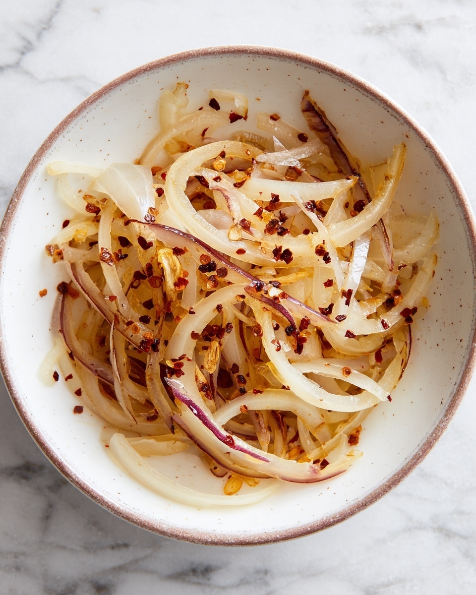 A white bowl contains thin slices of cooked onions with a mix of light brown and purple tones, spread loosely across the bottom. Among the onions, there are a few pale yellow, softened sticks of garlic or butter scattered unevenly. Small dark spices and red chili flakes are sprinkled around, adding texture and color contrast over the lightly browned surface of the bowl. The background has a white marbled texture. photo taken with an iphone --ar 4:5 --v 7