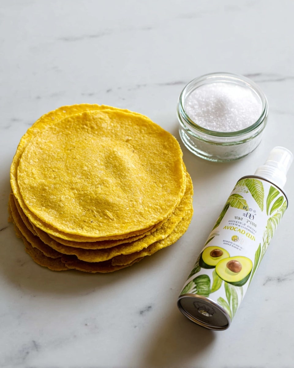 The image shows a stack of six yellow corn tortillas on the left, each with a slightly rough and textured surface, arranged in a neat pile on a white marbled surface. To the right of the tortillas, there is a small clear glass jar filled with white salt crystals. Below the jar, a can of avocado oil spray lies horizontally, with a white body decorated with green avocado and leaf illustrations and text labeling it as avocado oil spray. The scene is simple and clean with soft natural light. Photo taken with an iphone --ar 4:5 --v 7