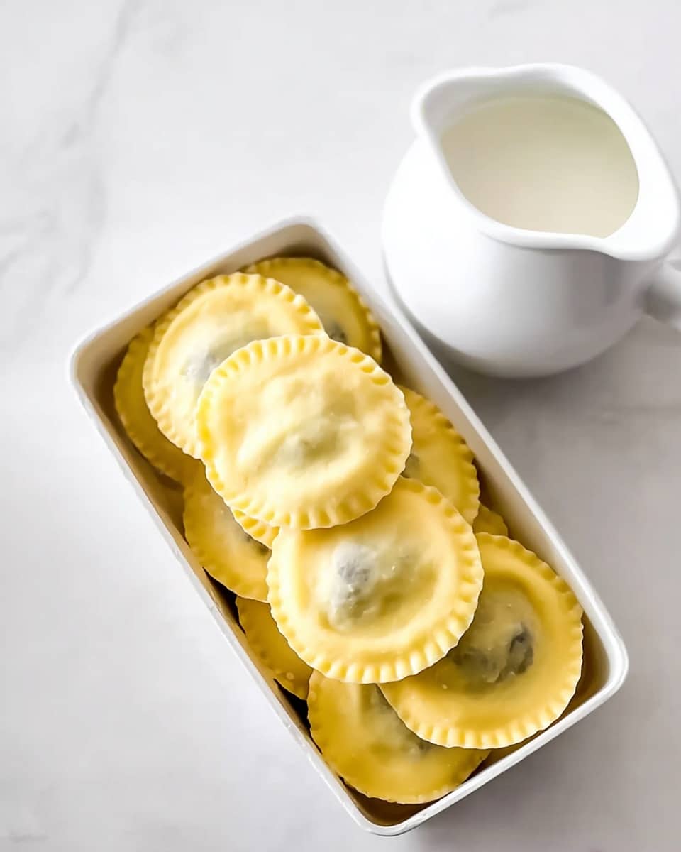 A red pot filled with a creamy white sauce with visible black pepper and red chili flakes, covering several round ravioli arranged closely together. The ravioli have a pale yellow color with a smooth texture, slightly overlapping each other. Scattered thin brown mushroom slices float in the sauce. A wooden spoon rests inside the pot, partially stirring the ravioli and sauce. The pot sits on a wooden surface replaced by a white marbled texture. Photo taken with an iphone --ar 4:5 --v 7