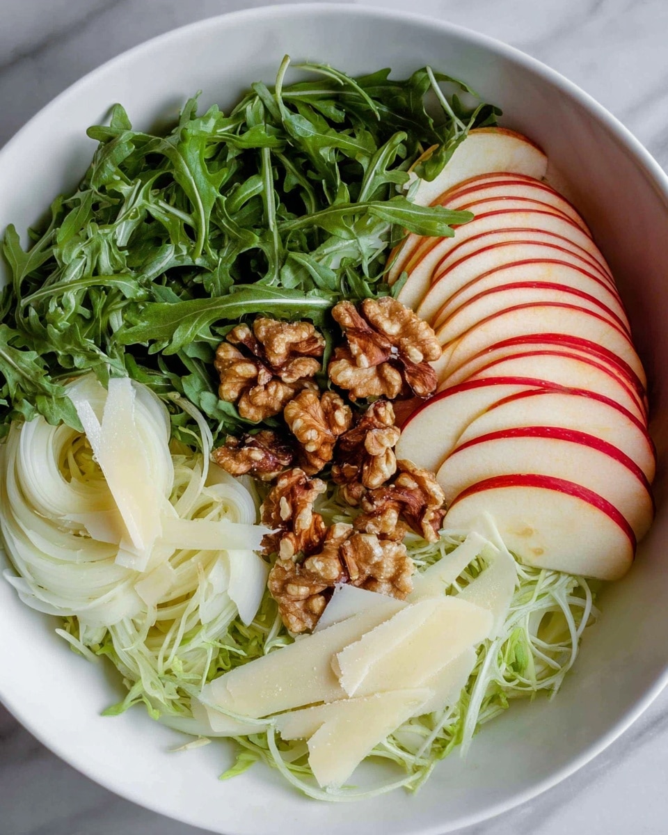 A white bowl filled with a fresh salad showing many thin layers of dark green arugula leaves spread throughout. There are thin slices of pale white fennel with light green tints, and thin red-skinned apple slices with white inside layered evenly over the greens. Scattered among the greens are light brown walnut pieces adding texture. Thin, pale yellow shaved cheese pieces are spread on top, with small green dill fronds sprinkled lightly all over. The salad looks fresh and colorful with small black pepper specks visible on top. The bowl rests on a white marbled texture. photo taken with an iphone --ar 4:5 --v 7