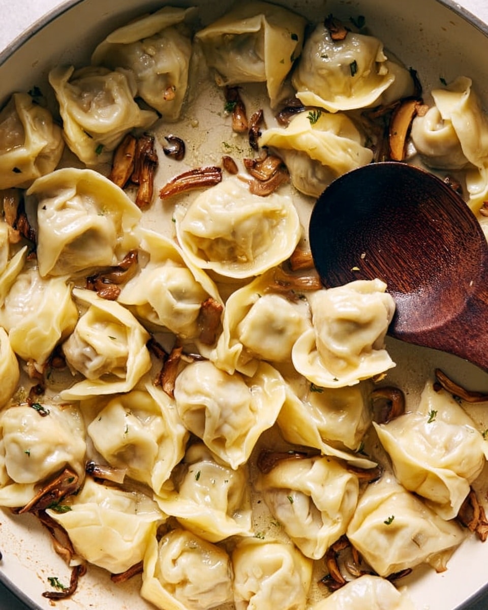The image shows light yellow dumplings cooking in a white pan with small brown mushroom strips scattered around. The dumplings have a wrinkled texture, and a dark wooden spoon is resting inside the pan on the right side. The dumplings are spread across the pan, with some overlapping and showing soft folds in their dough. The overall look is warm, soft, and slightly shiny from cooking oil or water. Photo taken with an iphone --ar 4:5 --v 7
