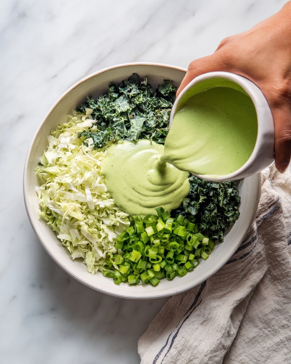A white bowl sits on a white marbled surface, filled with three distinct layers of chopped vegetables: light green shredded cabbage on the left, dark green chopped kale at the top right, and medium green chopped green onions with a mix of stalks and small pieces at the bottom right. A woman's hand is pouring a bright green creamy sauce onto the center of the vegetables, with the sauce creating a smooth, flowing texture as it lands in the bowl. A light-colored cloth with subtle stripes lies partially under the bowl. Photo taken with an iphone --ar 4:5 --v 7