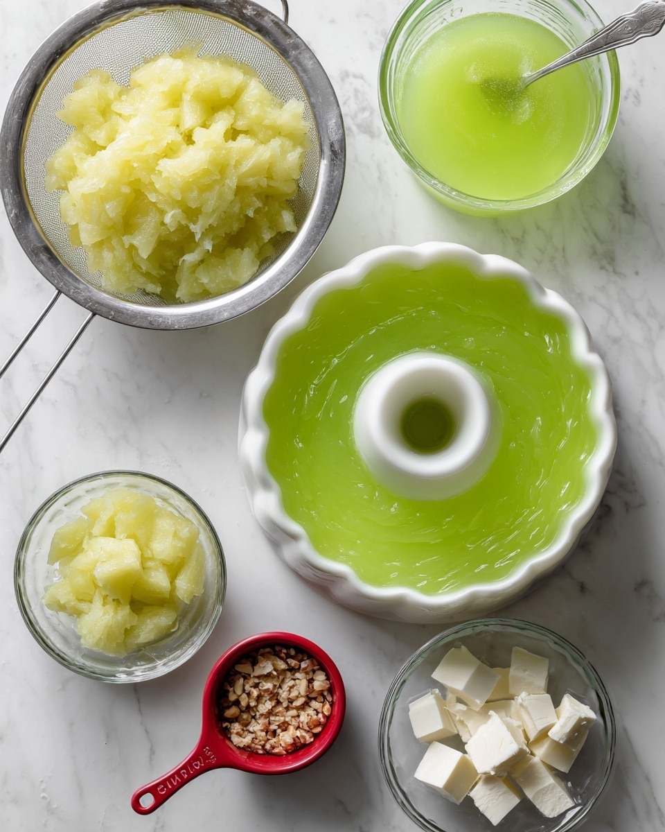 The image shows a top view of ingredients and tools for a green gelatin dessert on a white marbled surface. In the center, there is a white bundt mold filled with bright green gelatin, smooth and shiny in texture. To the left, a metal strainer holds mashed pale yellow pineapple with a rough, lumpy texture, set over a clear glass bowl. To the right, a glass measuring cup contains more green gelatin with a spoon inside, showing a smooth liquid texture. Below the mold, a small red measuring cup holds crushed nuts with a coarse texture, and next to it is a clear dish with several pieces of white, soft cream cheese. The setup looks clean and ready for assembly. Photo taken with an iphone --ar 4:5 --v 7