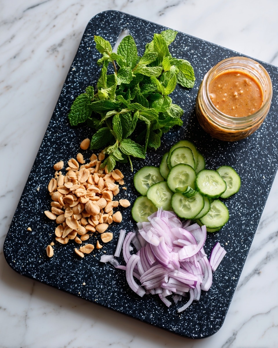 The image shows a black speckled cutting board on a white marbled surface. On the board, there is a small pile of roughly chopped peanuts in the center-left. To the left of the peanuts are some green leafy herbs and mint, while on the right, there are thinly sliced cucumber pieces arranged in a small pile. Above the cucumber slices, thinly sliced light purple onion strips are placed. On the far right side of the board, a transparent glass jar contains an orange-brown sauce or dressing. At the bottom edge, part of a woman's blue jeans is visible. Photo taken with an iphone --ar 4:5 --v 7