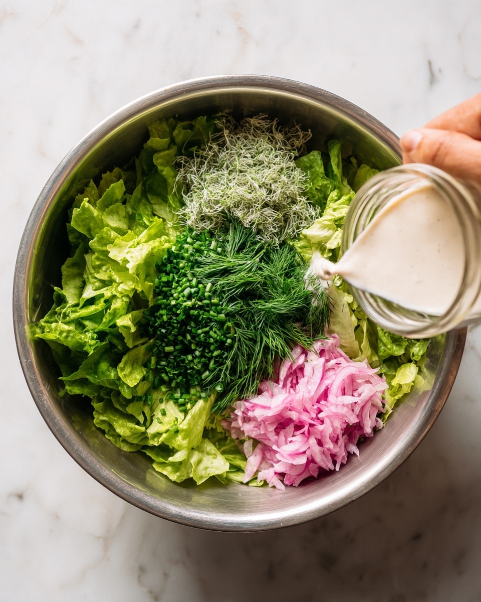 A large metal bowl sits on a white marbled surface, filled with layers of fresh green lettuce leaves at the bottom. On top of the lettuce, there are three distinct piles of herbs and vegetables: bright green chopped chives in the center, light green feathery dill to the left, and light pink pickled onions on the upper right side. A woman's hand is holding a glass jar pouring a creamy white liquid dressing over the salad from the right side of the image. The light softly highlights the freshness of each ingredient. photo taken with an iphone --ar 4:5 --v 7
