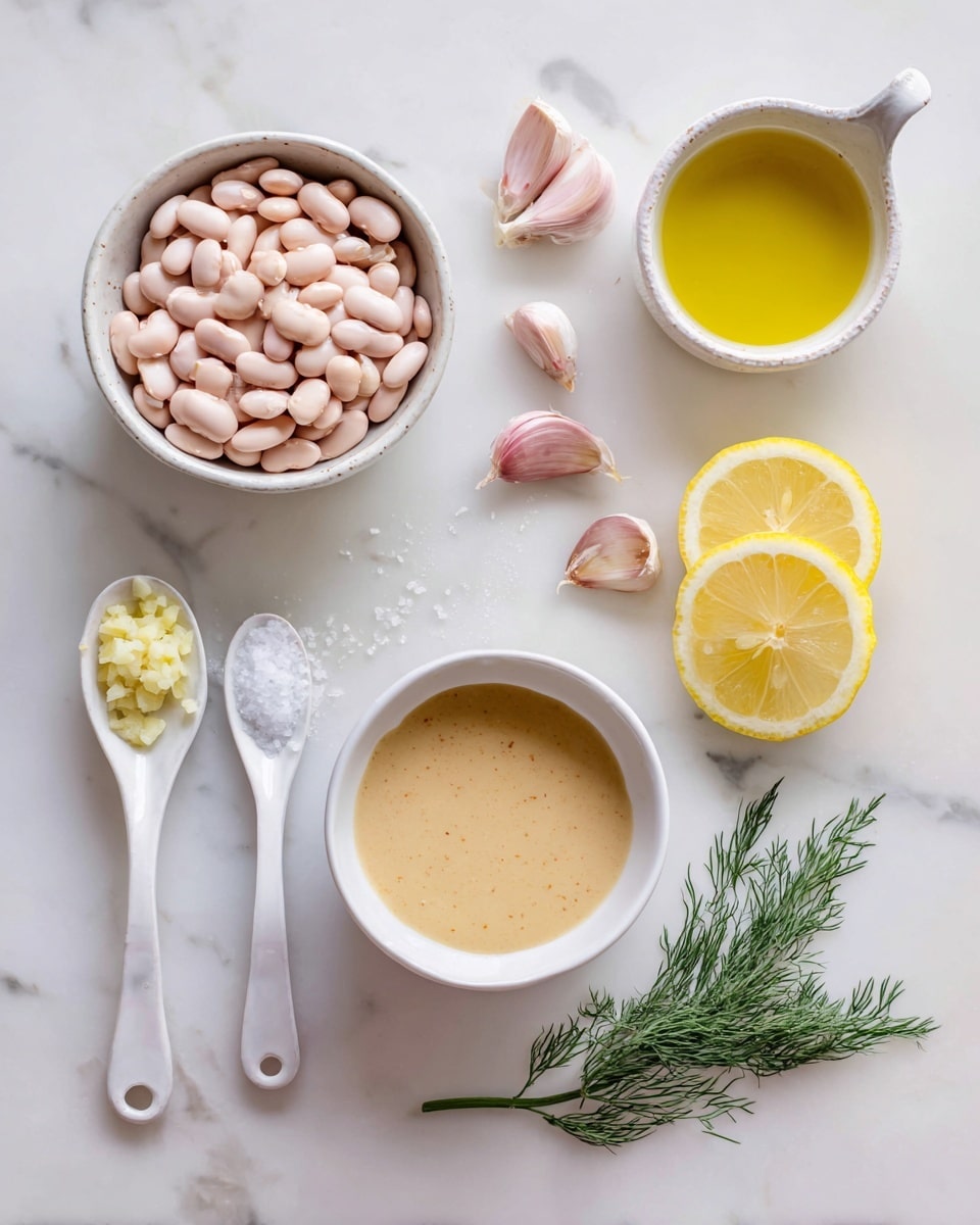 The image shows a top view of cooking ingredients arranged on a white marbled surface. In the middle left, there is a small white bowl filled with light pink beans. Below it, on the bottom right, there is a white bowl filled with a light brown creamy sauce. Above the beans, slightly to the right, a white bowl holds a golden-yellow liquid, likely oil. To the left, two white ceramic spoons lie parallel; one holds coarse salt and the other minced garlic, both creamy white with a speckled texture. On the right side, three lemon slices are stacked, showing bright yellow color with visible seeds. Above the lemon slices, five garlic cloves with pale pink peel are scattered. A few green dill sprigs with feathery leaves are placed at the extreme right edge. Photo taken with an iphone --ar 4:5 --v 7