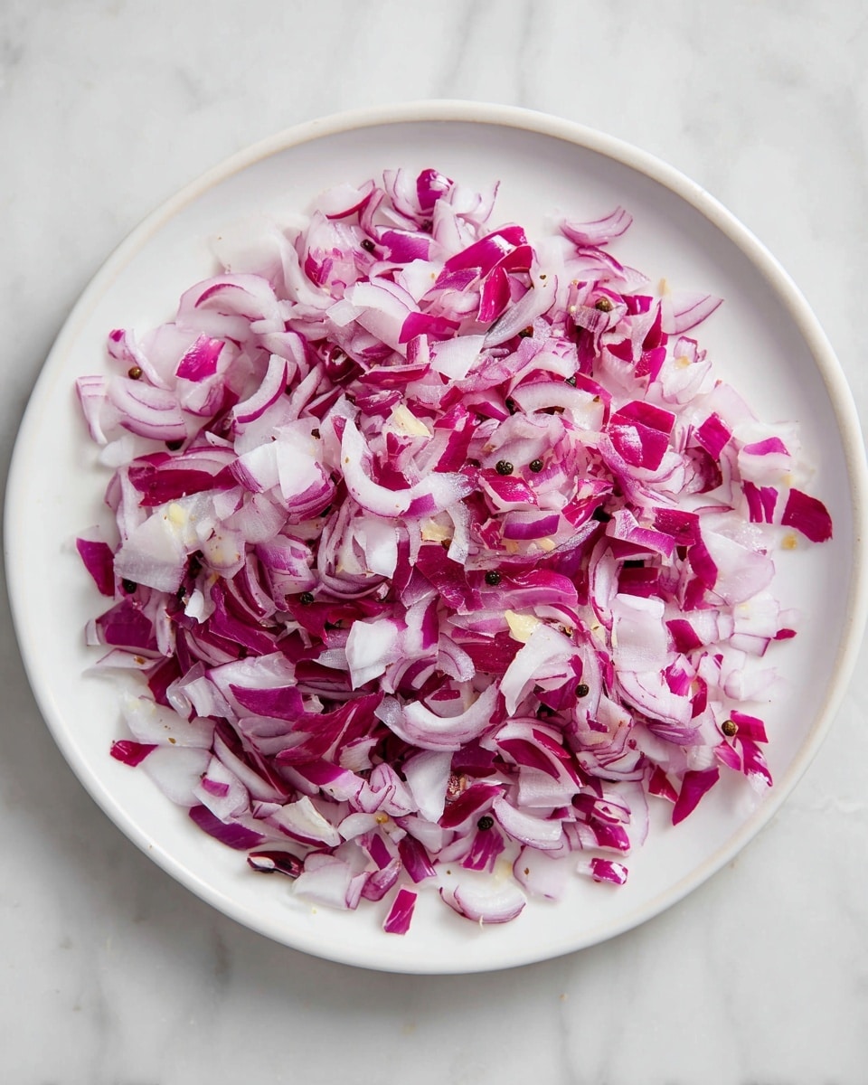 The image shows a close-up of a white plate with a single layer of finely chopped red onions scattered evenly across the surface. There are small bits of pale yellow ginger mixed in with the onions, adding texture and light color contrast. Tiny dark mustard seeds are sprinkled throughout, their round shapes visible between the onion pieces. The onions look fresh with sharp edges and some shine from natural moisture. The white plate sits on a white marbled background, keeping the focus on the detailed ingredients. Photo taken with an iphone --ar 4:5 --v 7