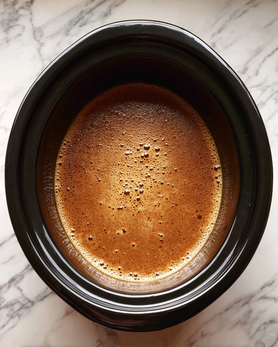 A black slow cooker filled with a single layer of brown, slightly frothy liquid broth is shown from above, placed on a white marbled surface, photo taken with an iphone --ar 4:5 --v 7
