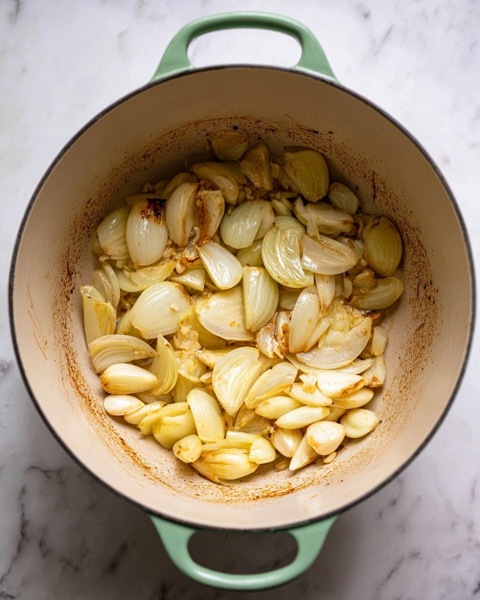 A round light green pot is shown from above, placed on a white marbled surface. Inside the pot, there are cooked pieces of onion and garlic. The onion pieces are light golden with some shiny texture, varying in size and irregular shapes, spread out around the bottom and sides of the pot. The garlic cloves are pale yellow, whole or halved, mixed with the onions. The bottom of the pot shows brown bits stuck from cooking, giving a rustic look to the scene. The pot’s interior is cream-colored with some brown stains from the cooked ingredients. Photo taken with an iphone --ar 4:5 --v 7