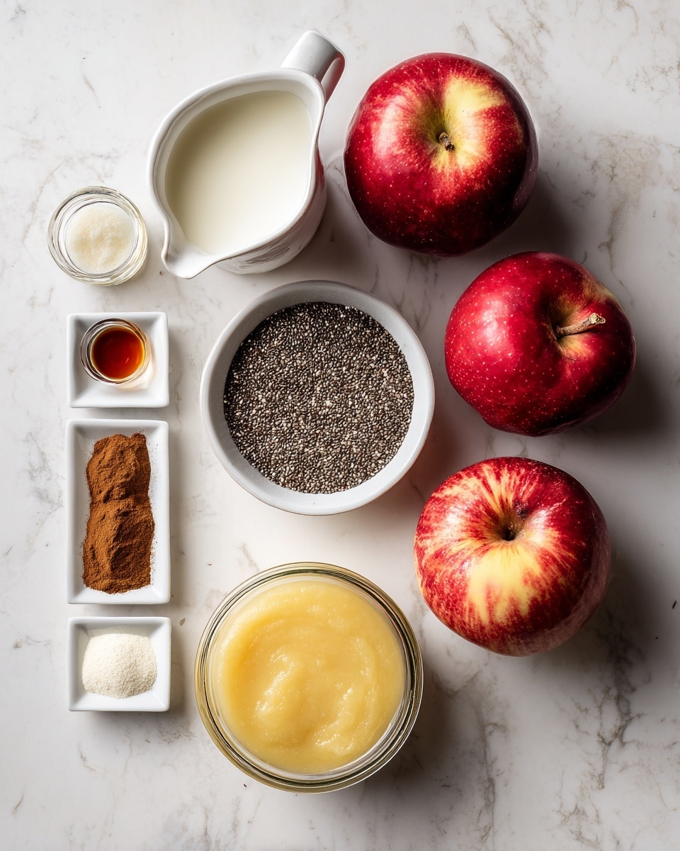 The image shows an overhead view of several fresh ingredients arranged neatly on a white marbled surface. There are two whole red apples placed on the right side, one with a darker red color and the other with a mix of red and light yellow tones. Above and to the right of the apples is a white bowl filled with dark chia seeds, showing a granular texture. In the center bottom is a small clear glass jar filled with a smooth apple sauce, golden yellow in color. To the left of the sauce jar is a glass bottle with a dark liquid inside, likely vanilla extract, and next to it sits a tiny clear container with a small amount of amber liquid. Above these is a small white pitcher holding a light white cream or milk. At the upper left corner of the image, two small rectangular white dishes hold brown spices, one dish with a cocoa-like powder and the other with a cinnamon-colored powder. Finally, there is a glass bottle filled with a white liquid, positioned near the center left, completing the set of ingredients. Everything is arranged on a clean white marbled surface. photo taken with an iphone --ar 4:5 --v 7