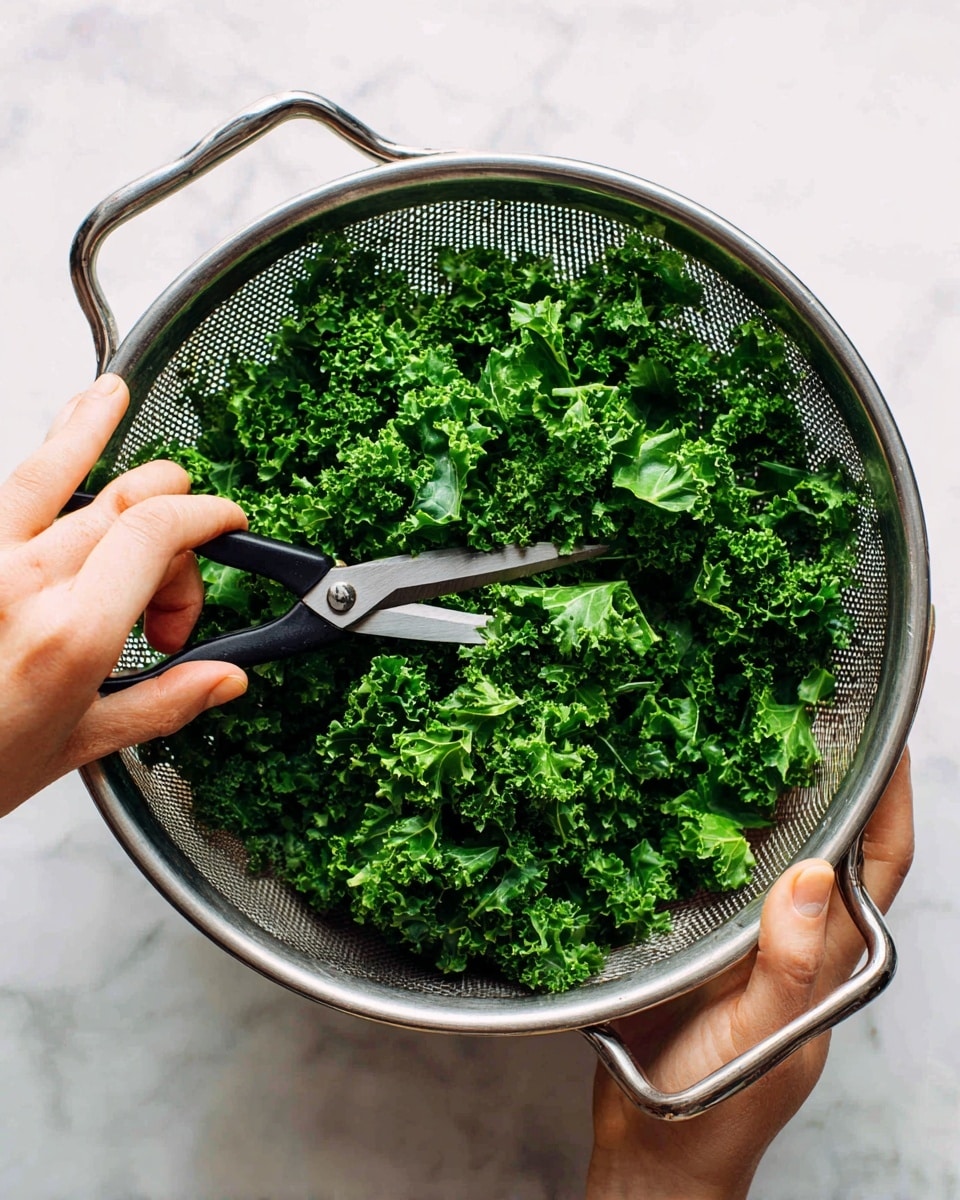 A metal colander is filled with bright green chopped kale pieces that have a slightly curly and leafy texture. The colander has two handles and is held by a woman's hand on the left side. Another woman's hand is using black-handled scissors to trim the kale inside the colander. The whole scene is set on a white marbled surface, giving a clean and fresh look. photo taken with an iphone --ar 4:5 --v 7