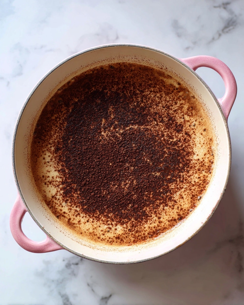 A round pink pot filled with smooth, dark brown chocolate liquid, showing soft swirls on the surface. The pot sits on a white marbled surface. In the background, there is a clear glass cup on the right and a white bowl with chocolate pieces at the back, along with a small green plant on the left. The scene is bright and clean with soft lighting photo taken with an iphone --ar 4:5 --v 7