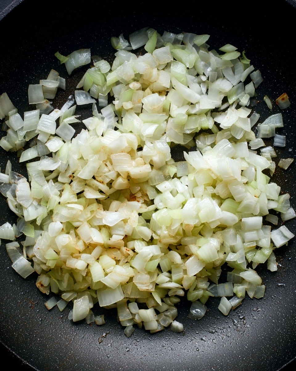 The image shows a close-up of a black pan with two groups of chopped onions spread out on its surface. The onions are diced into small pieces, with a mix of slightly translucent white and pale yellow colors, indicating they are being gently cooked but not browned yet. The texture looks soft with a little shine from the cooking oil. There is no other food present, just the onions in the pan. photo taken with an iphone --ar 4:5 --v 7