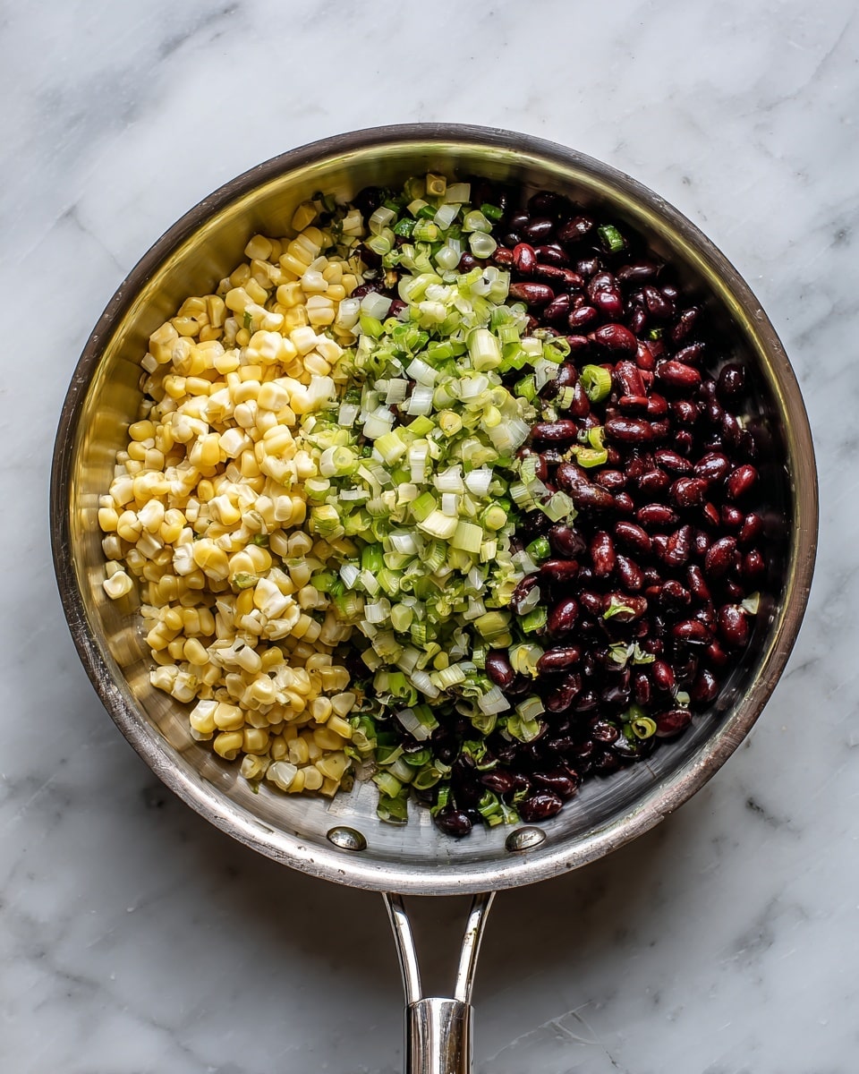 A shiny silver pan with a long handle holds three layers of food arranged side by side inside it: pale yellow corn kernels on the right, dark reddish-brown beans in the center, and small pale green and white chopped green onions spread on top, mostly over the beans and some over the corn. The pan sits on a white marbled surface, with light coming from above, showing the smooth and glossy colors of the ingredients clearly. Photo taken with an iphone --ar 4:5 --v 7