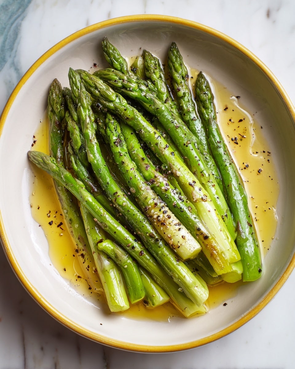 A white bowl with a yellow rim holds fresh green asparagus spears laid side by side, some overlapping. The asparagus has a shiny texture from being drizzled with golden olive oil that pools slightly at the bottom. Small black pepper flakes are sprinkled over the green stalks, adding a speckled contrast. The bowl sits on a white marbled surface with some blue hues around, making the green asparagus and yellow rim stand out clearly. photo taken with an iphone --ar 4:5 --v 7