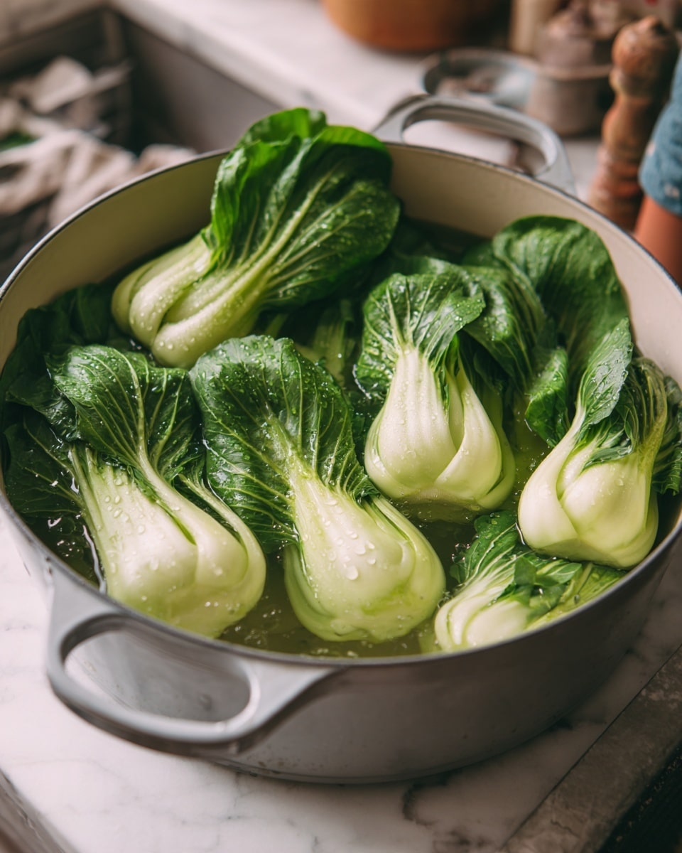 A large light gray pot filled with water holds several fresh bok choy. The bok choy has bright green leaves with some water droplets on them and pale white-green stems. The pot has a simple metal handle and is sitting on a white marbled surface. In the blurred background, part of a person's arm and some kitchen items are visible. Photo taken with an iphone --ar 4:5 --v 7