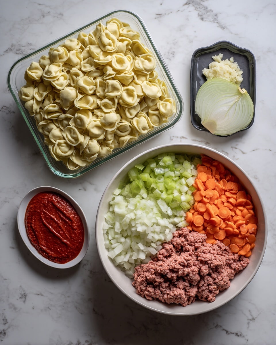 The image shows an arrangement of food ingredients on a white marbled surface. On the left, there is a clear container filled with many small, pale yellow tortellini pasta pieces. In the center right, there is a large white bowl divided into four parts by the ingredients inside: finely chopped light green celery, white onions, and orange carrots. Above the bowl, a small white plate holds a small pile of minced garlic. Below and to the left of the large bowl is a small oval white dish with two dollops of thick red tomato paste. At the bottom right corner, a black container has lines of raw ground meat. Part of a transparent green bottle is visible on the far left near the edge of the image. photo taken with an iphone --ar 4:5 --v 7
